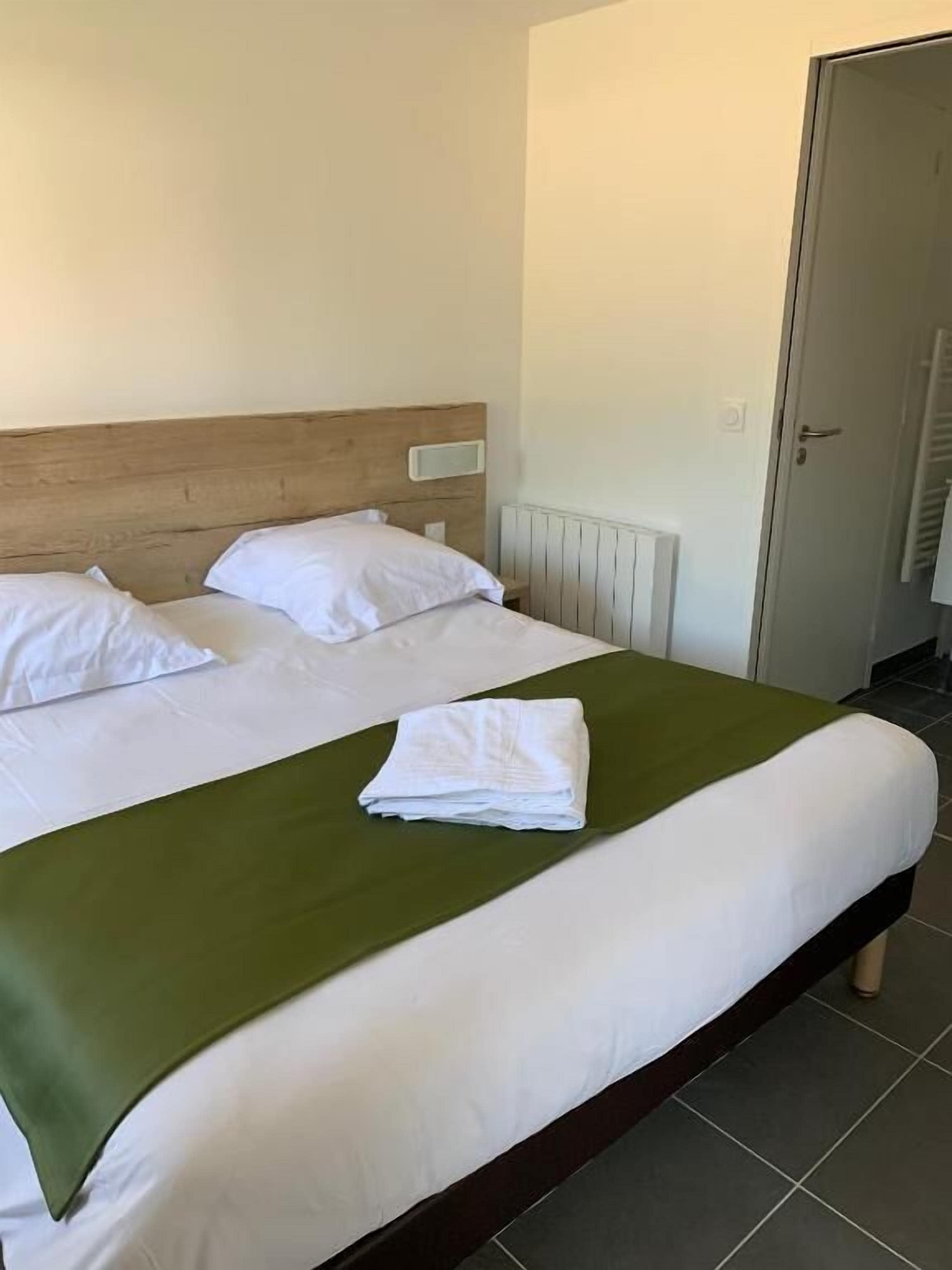 Un letto rifatto con lenzuola bianche e una coperta verde, una testiera in legno e un termosifone bianco.