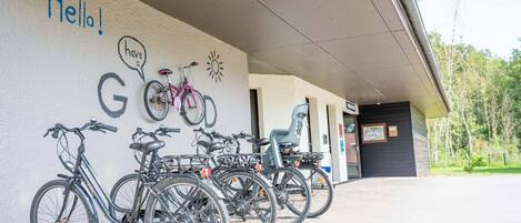Une rangée de vélos est garée contre un mur, avec les inscriptions « Bonjour ! » et « Passez une bonne journée ! ».
