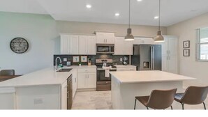 Une cuisine moderne avec des armoires blanches, des appareils en acier inoxydable et des luminaires suspendus.