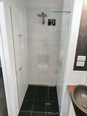 A small, enclosed shower area with a glass door, a black tiled floor, and a metal sink with a faucet. - Fernbrook Escape Secluded and Serene (Cockatoo)