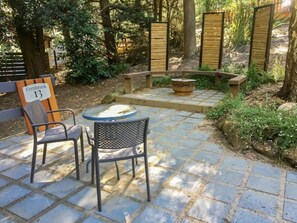 An outdoor patio area with stone flooring, a round table, two chairs, a fire pit, and a sign indicating 'Fernbrook 13'. - Fernbrook Escape Secluded and Serene (Cockatoo)