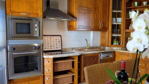 A kitchen with wooden cabinets, a built-in oven, a microwave, and a wine rack. - Atico de Lujo (Guia de Isora)