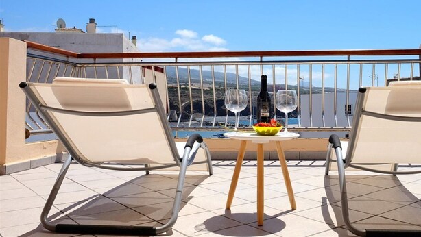 A balcony with two chairs, a table with a bottle and glasses, and a view of the sea and mountains. - Atico de Lujo (Guia de Isora)