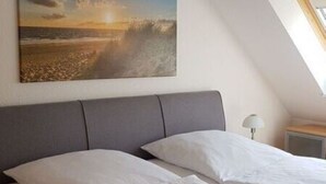 A bedroom with a bed, a headboard, and a painting of a beach scene. - Waldstr. 34 Wo.05 - Wo.05 (Kühlungsborn)