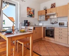 Een keuken met houten kastjes, een betegelde spatwand, een magnetron en een koffiezetapparaat.