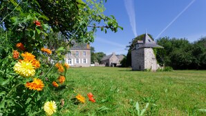 Ein grünes Feld mit einem Steinhaus und einem großen Gebäude im Hintergrund.