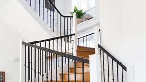 Eine Treppe mit schwarzen Geländern und Holzstufen in einem hellen Raum mit weißen Wänden und Fliesenboden.