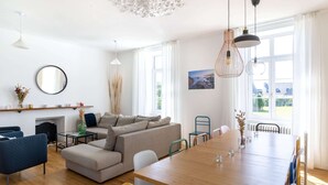 Ein modernes Wohnzimmer mit Sofa, Sesseln, Esstisch und Kamin.
