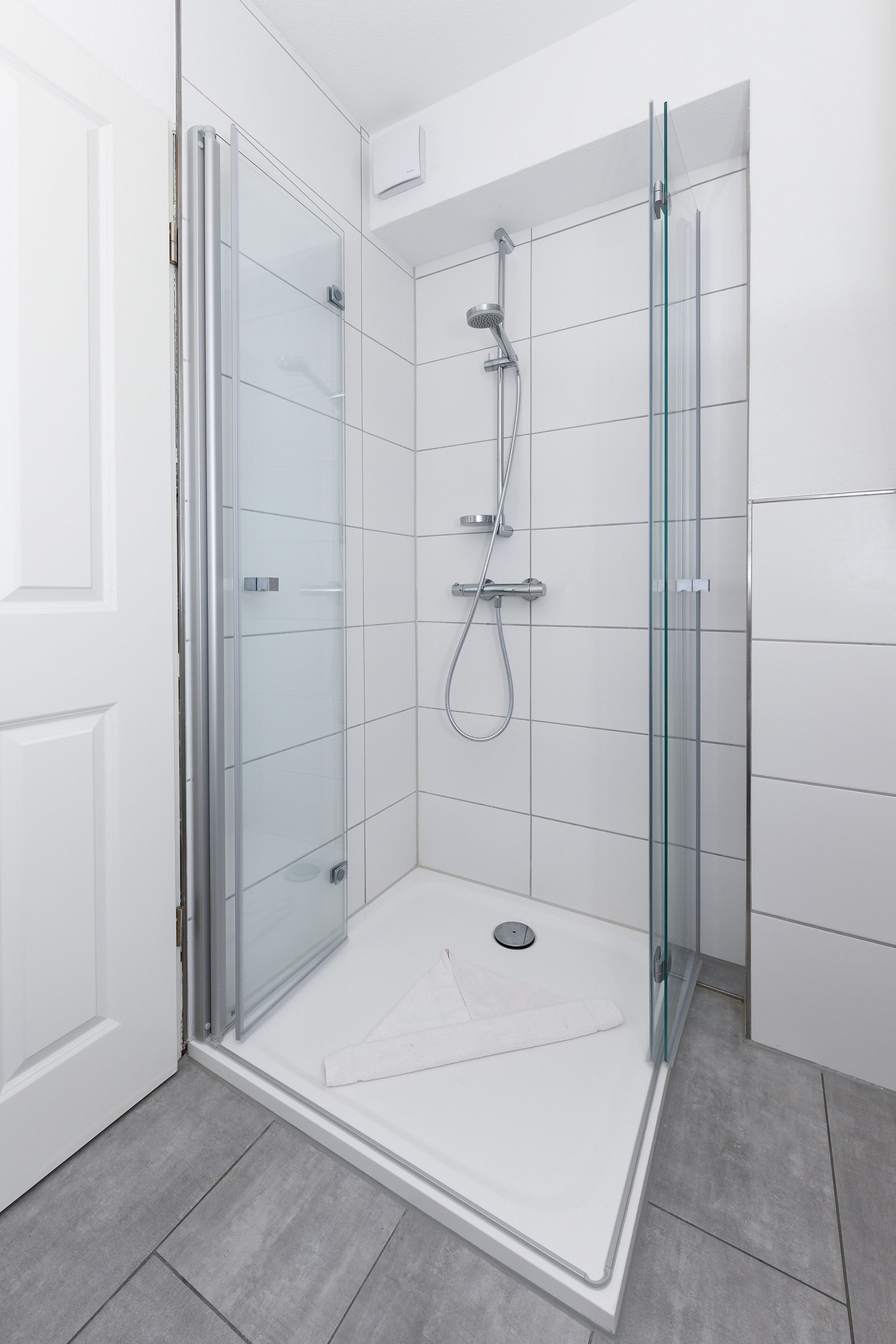 A modern shower with glass doors, a handheld showerhead, and a wall-mounted faucet.