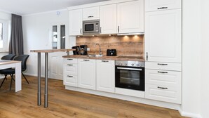 A modern kitchen with white cabinets, a wooden countertop, a built-in microwave, a coffee maker, and an oven. - Ferienwohnung Juist - Ferienwohnungen Min Huus (Neuharlingersiel)