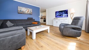 A modern living room with a grey sofa, a white coffee table, and a grey armchair. - Ferienwohnung Juist - Ferienwohnungen Min Huus (Neuharlingersiel)