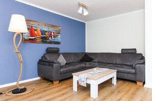 A living room with a dark grey sofa, a wooden coffee table, a floor lamp, and a painting of sailboats on a blue wall.