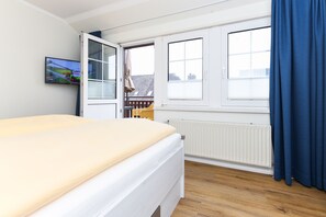 Une chambre à coucher avec un lit, une fenêtre avec des stores, un radiateur et un téléviseur fixé au mur.