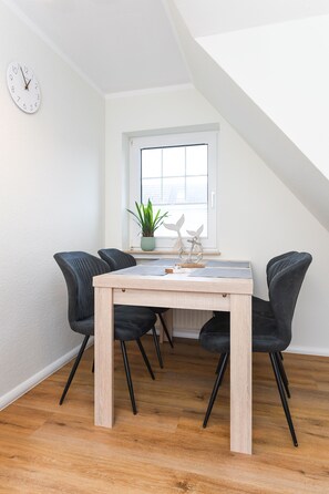 A dining area with a wooden table, black chairs, a potted plant, and a window with a view.