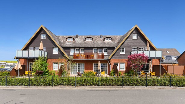 A two-story house with a balcony, a fenced garden, and a clear blue sky. - Ferienwohnung Norderney - Ferienwohnungen Min Huus (Neuharlingersiel)