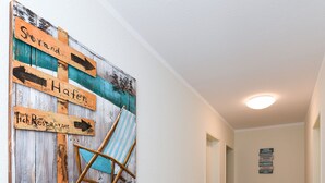 A hallway with wooden flooring, a wall-mounted sign with directional arrows, and a blue-striped chair. - Ferienwohnung Norderney - Ferienwohnungen Min Huus (Neuharlingersiel)