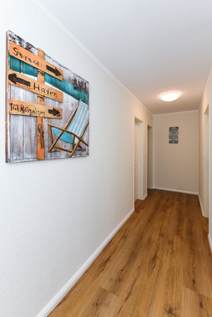 Un couloir doté d’un plancher en bois, d’un panneau mural avec des flèches indiquant la direction, et d’une chaise à rayures bleues.