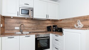 A modern kitchen with white cabinets, a wooden countertop, a microwave, a coffee maker, and an oven. - Ferienwohnung Norderney - Ferienwohnungen Min Huus (Neuharlingersiel)