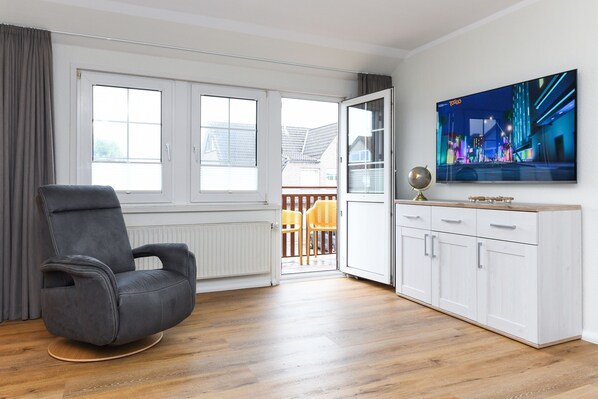 A modern living room with a grey leather chair, a white cabinet, and a flat-screen TV on the wall.