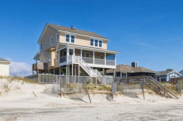 Beachfront vacation home with elevated design and private beach access via wooden walkway.