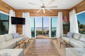 A modern living room with a ceiling fan, two sofas, a coffee table, and a large window with a view of the beach. - Exquisite Oceanfront Oasis: Immerse in Luxury with Pool & Putting Green! (Folly Beach)