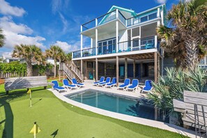 A two-story building with a swimming pool, outdoor seating, and palm trees. - Exquisite Oceanfront Oasis: Immerse in Luxury with Pool & Putting Green! (Folly Beach)