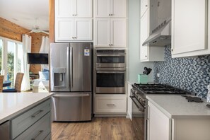A modern kitchen with stainless steel appliances, white cabinetry, and a tiled backsplash. - Exquisite Oceanfront Oasis: Immerse in Luxury with Pool & Putting Green! (Folly Beach)