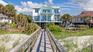 A beachfront property with a wooden boardwalk leading to a two-story building with balconies. - Exquisite Oceanfront Oasis: Immerse in Luxury with Pool & Putting Green at this (Folly Beach)