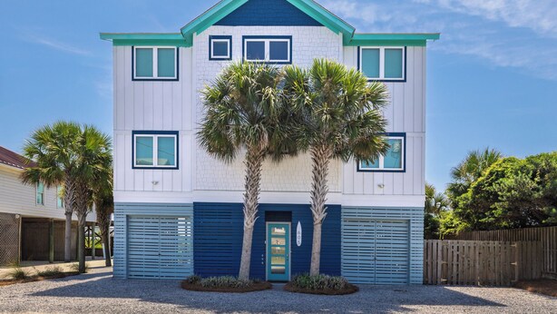 A two-story building with a blue and white exterior, a front door, and two palm trees in the driveway. - Exquisite Oceanfront Oasis: Immerse in Luxury with Pool & Putting Green at this (Folly Beach)