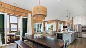 A spacious kitchen with a central island, a dining area with a wooden table, and a view of the ocean through large windows. - Exquisite Oceanfront Oasis: Immerse in Luxury with Pool & Putting Green at this (Folly Beach)