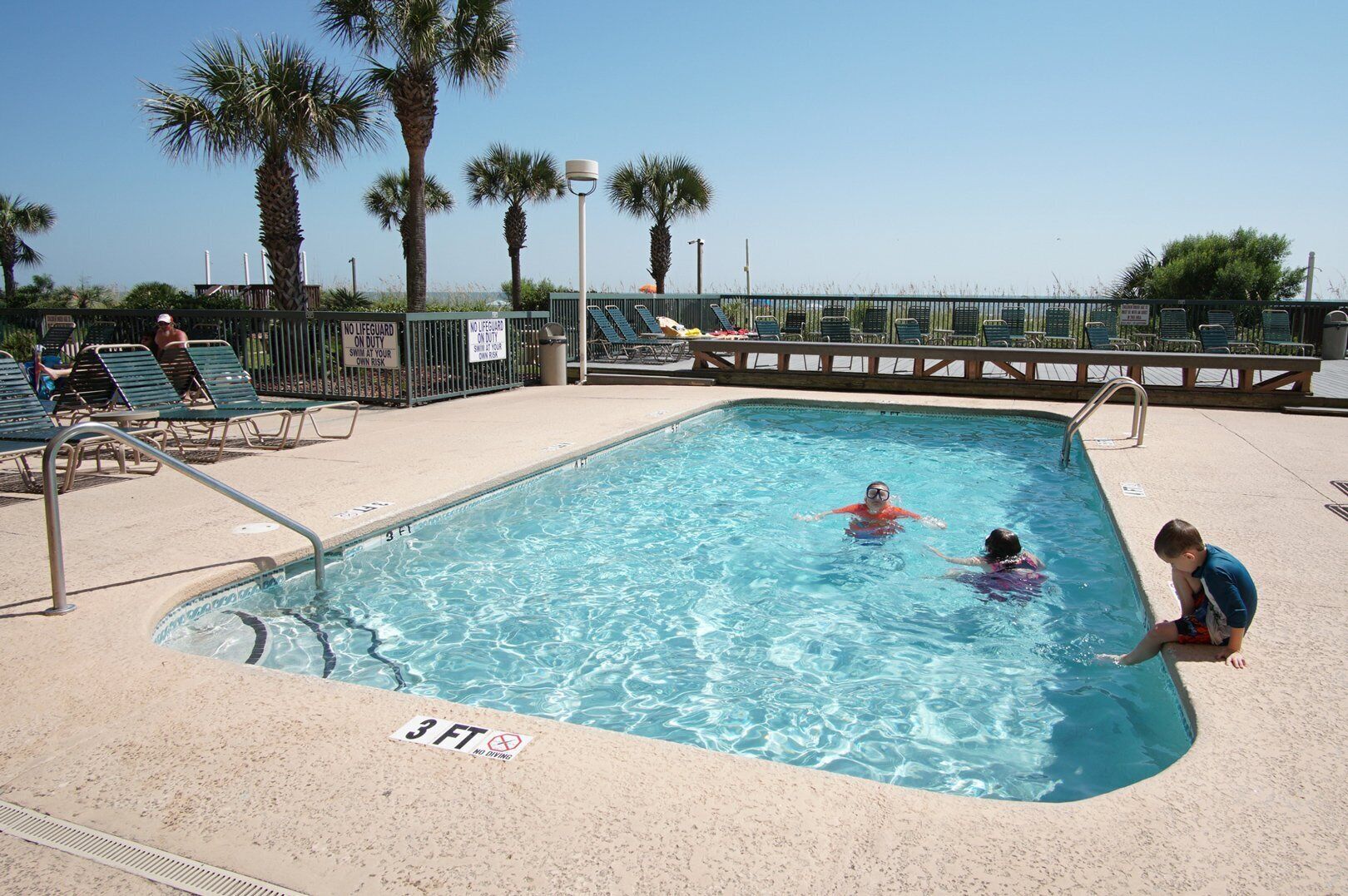 A swimming pool with a lifeguard station, lounge chairs, and a no diving sign.