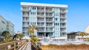 A multi-story hotel with balconies, a wooden boardwalk, and palm trees. - Direct ocean front condo with stunning renovations & updated "coastal chic" decor! (North Myrtle Beach)
