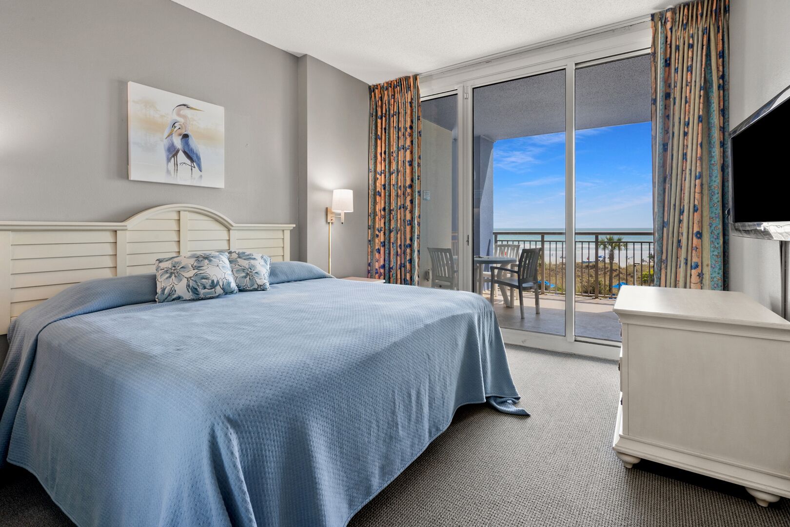 Habitación de hotel con cama, escritorio, silla, televisor y balcón con vistas.