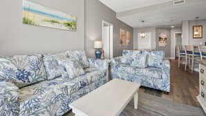 A living room with two sofas, a coffee table, and a painting on the wall. - Oceanfront luxury condo w/pools, lazy river, fitness center, sky deck and more (North Myrtle Beach)