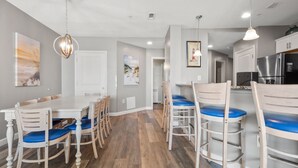 A modern kitchen with stainless steel appliances, a dining area with wooden chairs and blue cushions, and a hallway with a white door. - Oceanfront luxury condo w/pools, lazy river, fitness center, sky deck and more (North Myrtle Beach)