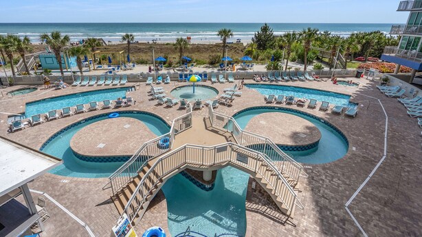 A pool area with multiple swimming pools, lounge chairs, and a beach view. - Oceanfront luxury condo w/pools, lazy river, fitness center, sky deck and more (North Myrtle Beach)
