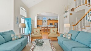 A spacious living room with two blue sofas, a coffee table, and a kitchen in the background. - Elegant, Luxury Home w/Private Pool & Easy Beach Access-North Myrtle Beach Rental (North Myrtle Beach)