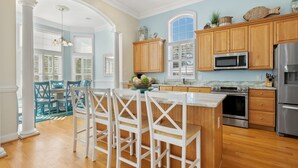 A kitchen with wooden cabinets, a stainless steel refrigerator, and a central island with bar stools. - Elegant, Luxury Home w/Private Pool & Easy Beach Access-North Myrtle Beach Rental (North Myrtle Beach)