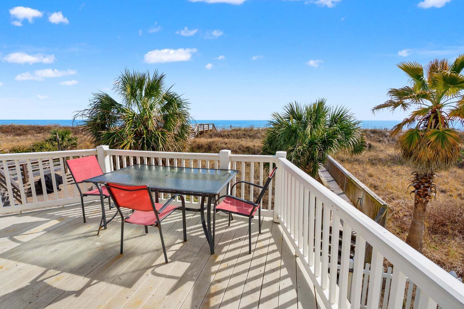 Een terras met tafel en stoelen, uitkijkend op een strand met palmbomen en de oceaan.
