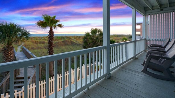 A wooden deck with a railing, palm trees, and a view of the beach. - Luxurious oceanfront home with private pool, putting green, private beach access and more (North Myrtle Beach)