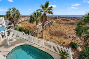 A pool area with a white fence, palm trees, and a view of the beach.