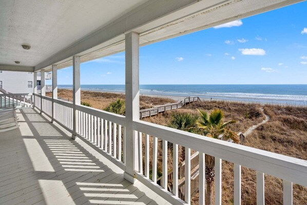 A covered porch with a view of the beach and ocean.