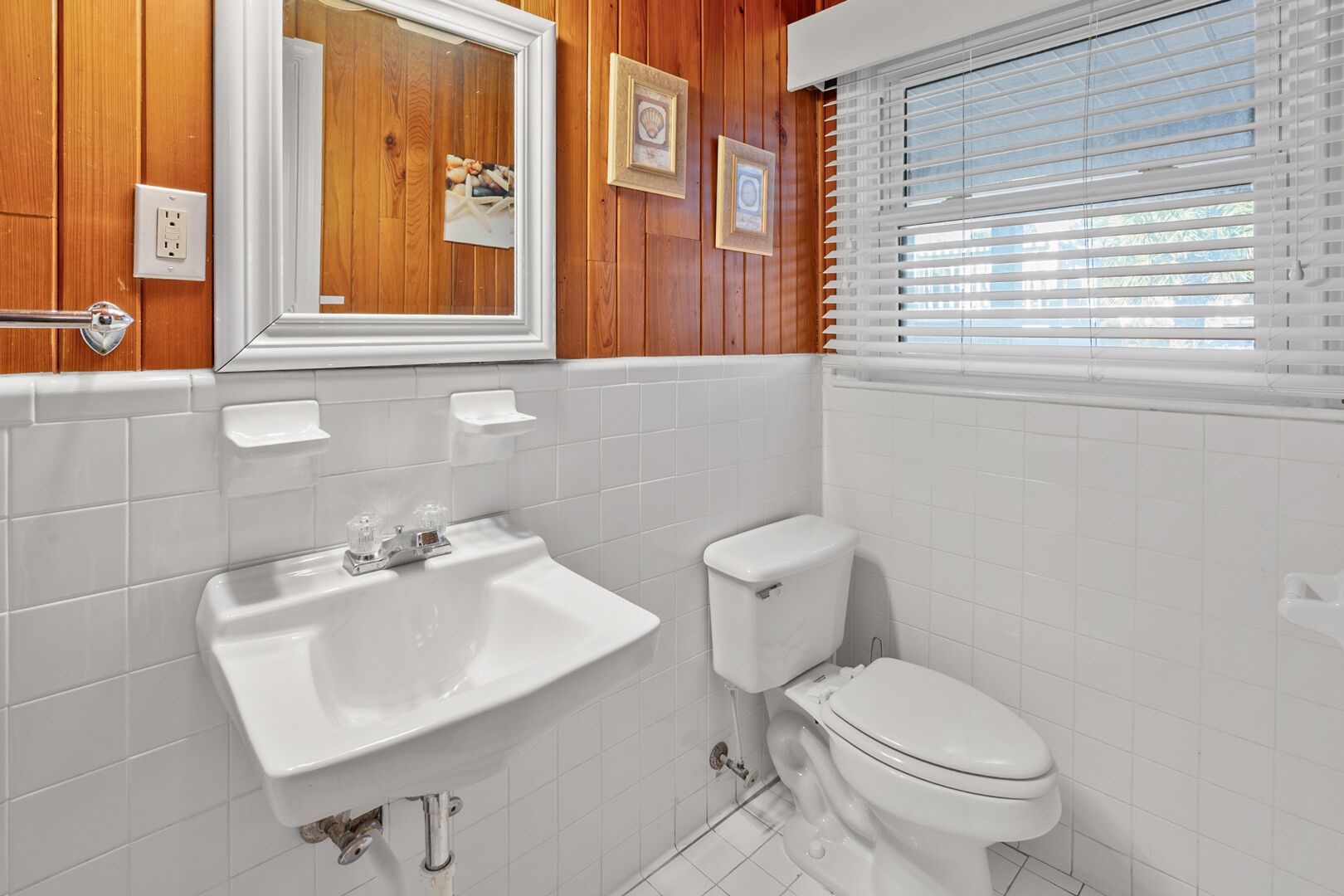A bathroom with a white sink, toilet, and window with blinds.