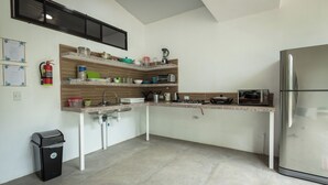 Una cocina compacta con un refrigerador de acero inoxidable, un horno empotrado y un microondas. Hay estantes de madera sobre la encimera con diversos utensilios de cocina.