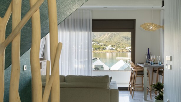 Una sala moderna con sofá, mesa de comedor y sillas, vista a un lago y montañas, y un balcón con barandilla.