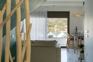 Una sala moderna con sofá, mesa de comedor y sillas, vista a un lago y montañas, y un balcón con barandilla.