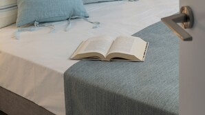 Una cama bien hecha con almohadas azules, un libro sobre la cama y una pared de piedra al fondo.