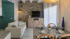 Una sala de estar moderna con una pared de piedra, un televisor, una mesa de comedor con platos y vasos, y un sofá con cojines.