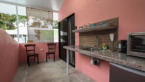 Cocina compacta con encimera de granito, lavamanos de acero inoxidable y microondas integrado. Hay dos sillas de madera y una ventana con vistas a zonas verdes.