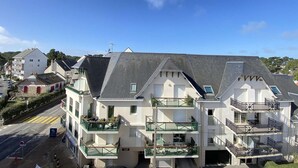 A multi-story residential building with balconies, a clear sky, and a road in the foreground.